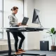 A person stands comfortably at a modern ergonomic standing desk, working on a laptop, demonstrating improved posture and productivity.