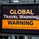 A digital display at an airport showing a 'Global Travel Warning' advisory, highlighting the immediate impact of the new virus outbreak on international travel.
